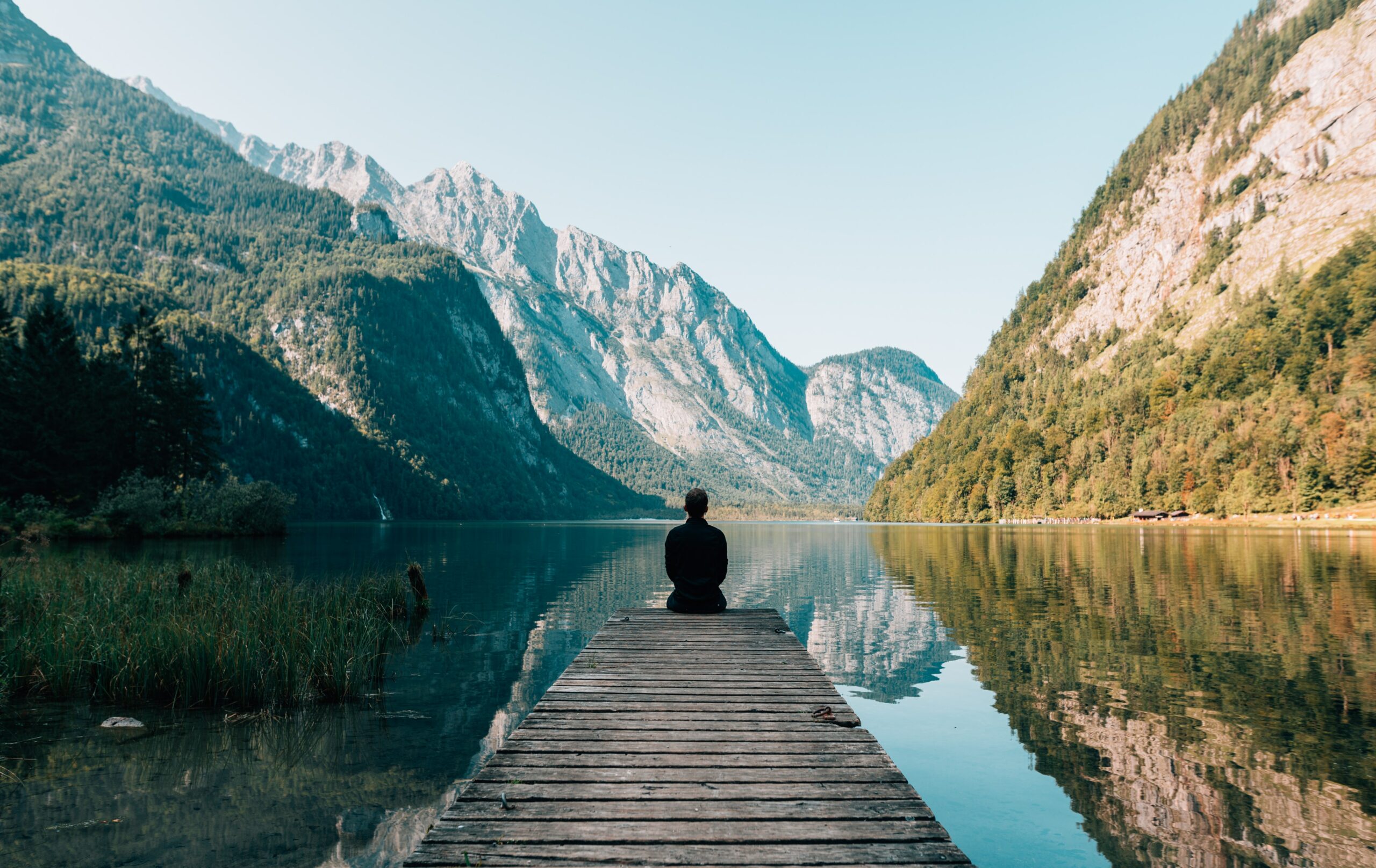 man sitting at the end of a dock looking onto a lake